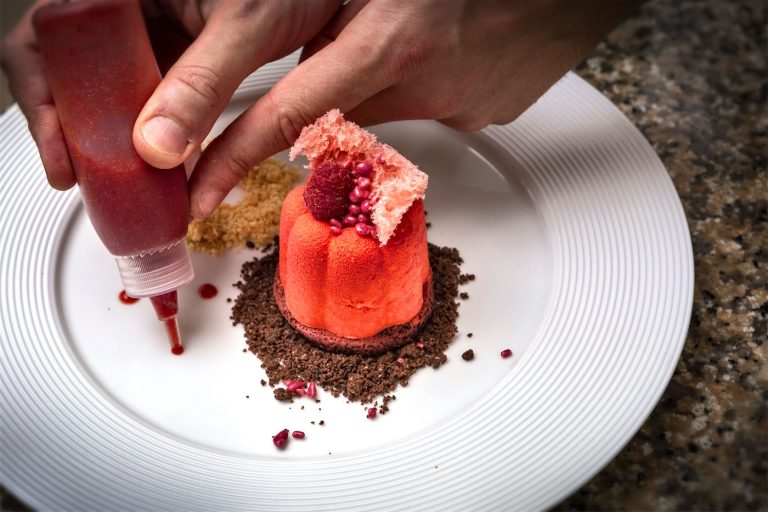 uno chef guarnisce con mousse ai frutti rossi un dessert su