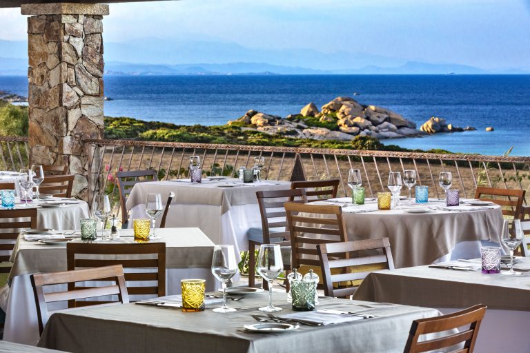 Tavoli apparecchiati su una veranda con vista sul mare e la Corsica sullo sfondo