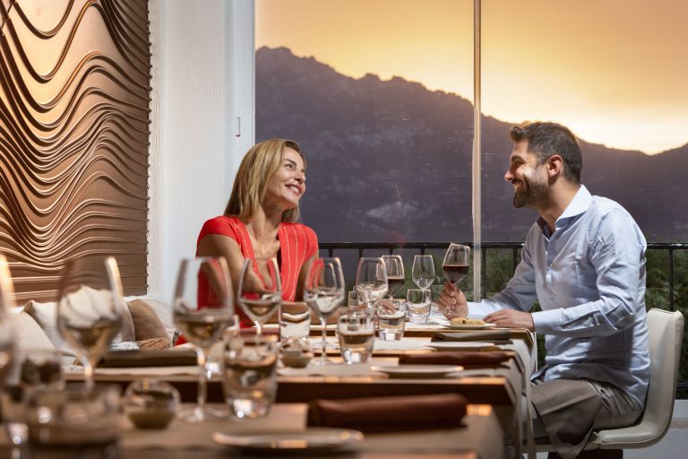 Due clienti seduti al tavolo di un elegante ristorante si guardano e sorridono mentre uno di loro tiene in mano un calice di vino