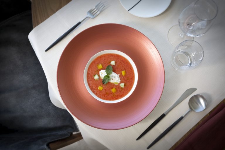 Un piatto di ceramica pregiata, con al centro un altro piatto con una zuppa di cucina gourmet, fotografata dall'alto