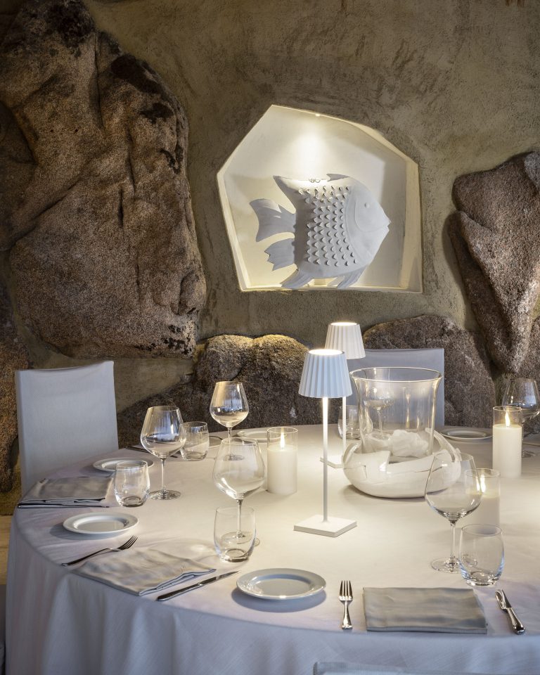 Un tavolo apparecchiato in modo elegante di fronte ad un muro in pietra con una scultura in ceramica bianca