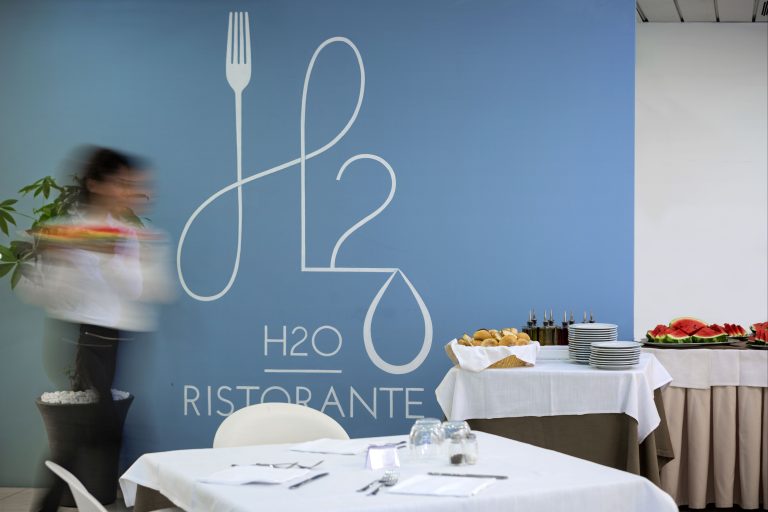 Tavoli apparecchiati, un buffet con pane e frutta per la colazione ed una cameriera che passa