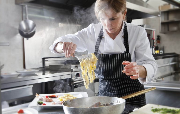 Una cuoca scola e prepara una porzione di pasta ai frutti di mare