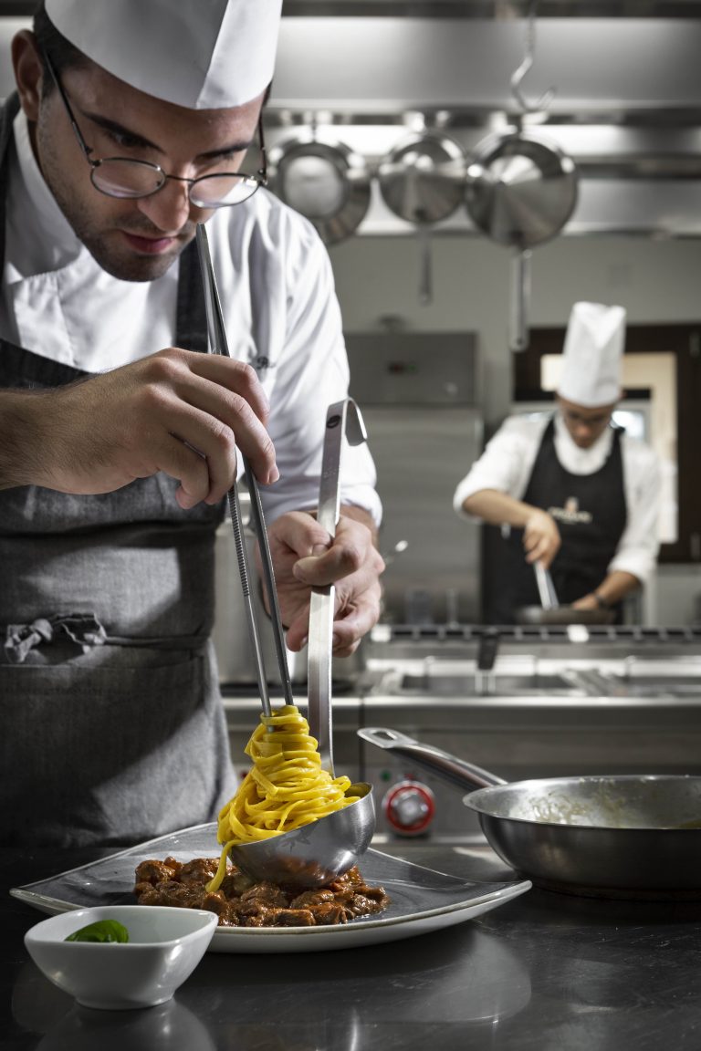 un cuoco prepara e poggia una porzione di spaghetti su un piatto con del condimento