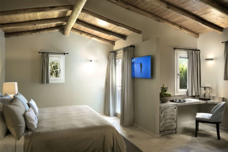 una ampia stanza da letto matrimoniale, con un angolo scrittura, un tetto spiovente in legno e finestre che si aprono su un giardino verde