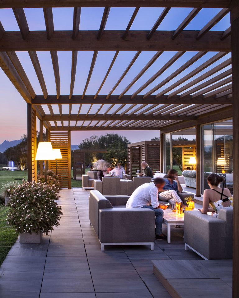 Clienti seduti su eleganti poltroncine e divanetti all'aperto, sotto una moderna pergola