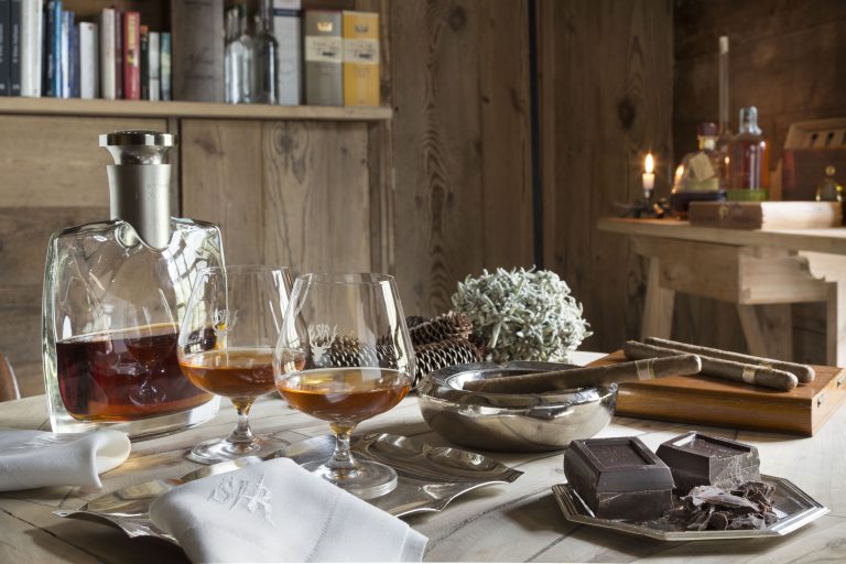Due bicchieri di cognac, cioccolato fondente e sigari poggiati su un tavolo in legno