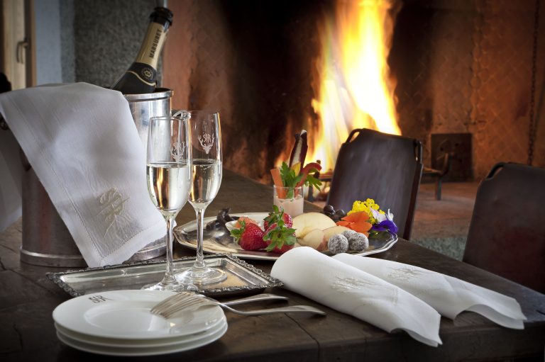 Calici di champagne, un vassoio con fragole e frutta assortita ed alcuni piatti vicino ad un camino acceso